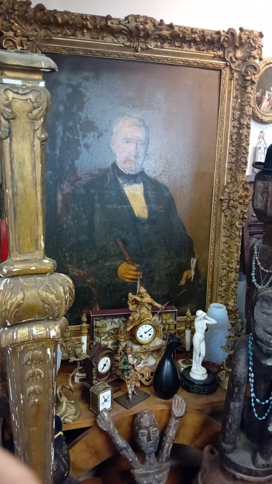 Portrait ancien dans un cadre doré orné, entouré d'objets religieux et anciens divers sur une étagère.