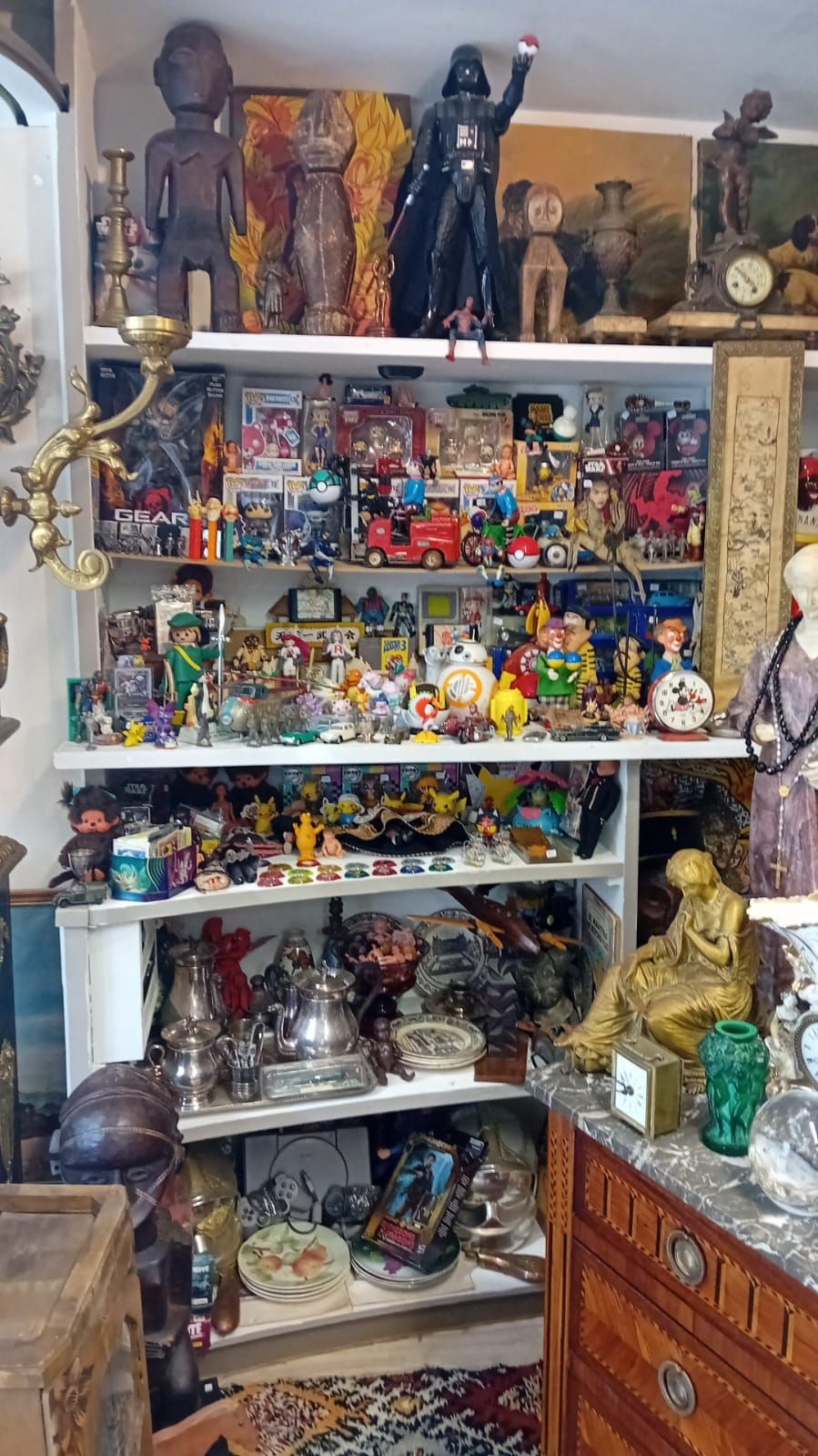 Des étagères remplies de jouets, de figurines, d'antiquités et d'objets de décoration ; on y trouve notamment une figurine de Dark Vador et une statue en or.