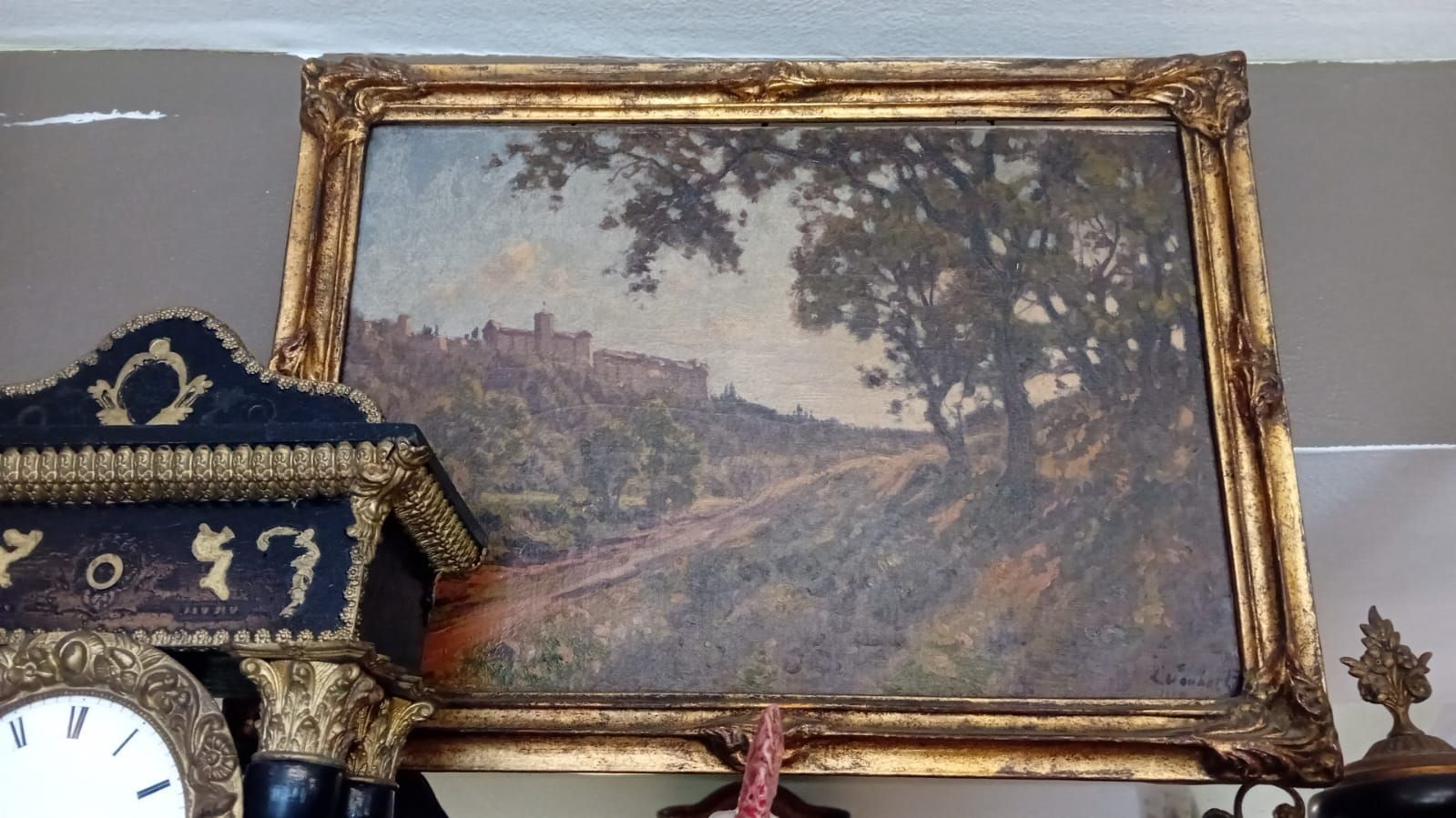 Tableau de paysage sous cadre doré, représentant une colline, des arbres et des bâtiments.