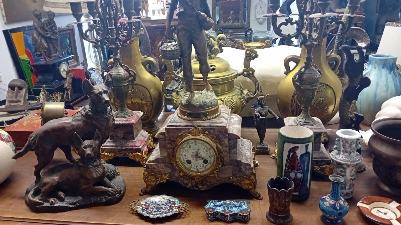 Vitrine d'un magasin d'antiquités présentant des horloges, des vases, des figurines et des bougeoirs.