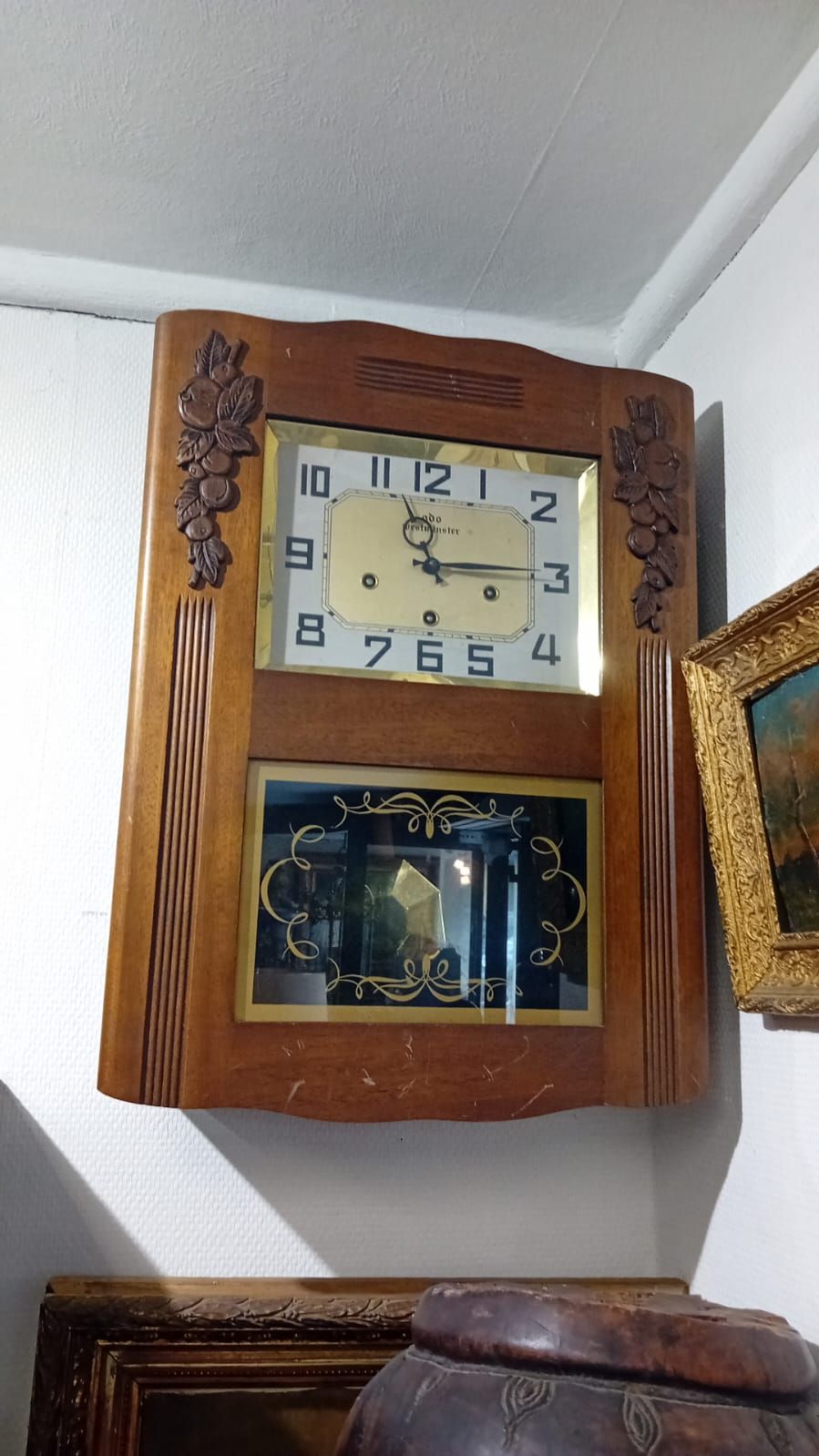 Horloge murale en bois avec cadran et pendule dorés, entourée d'une bordure décorative.