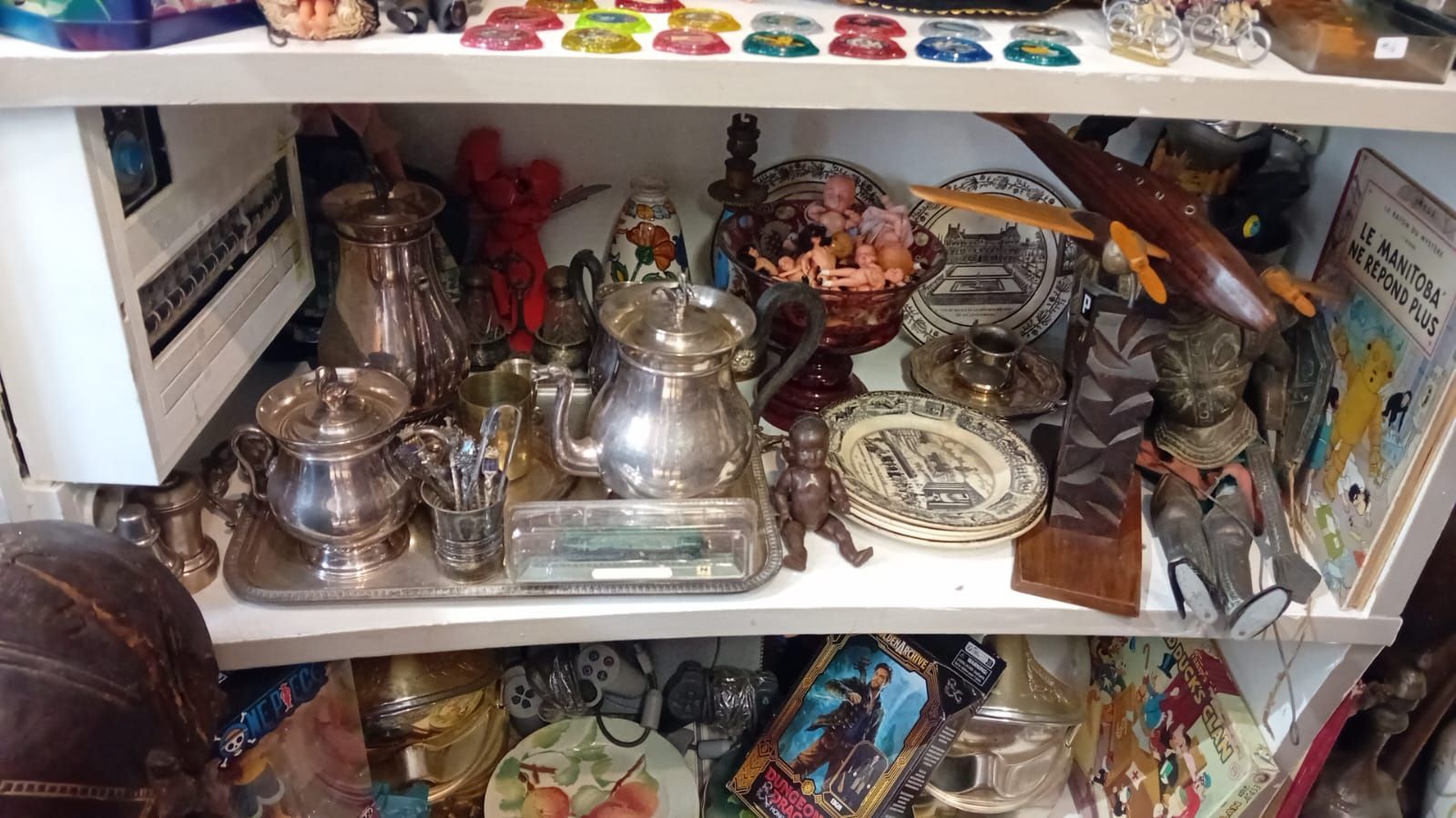 Des étagères remplies d'objets anciens, notamment de l'argenterie, des objets en verre et des assiettes décoratives.