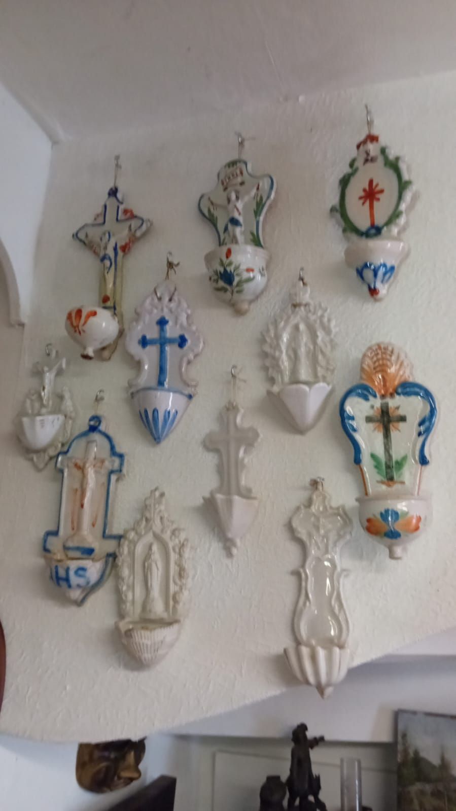 Collection de bénitiers en céramique finement ouvragés, accrochés à un mur blanc.