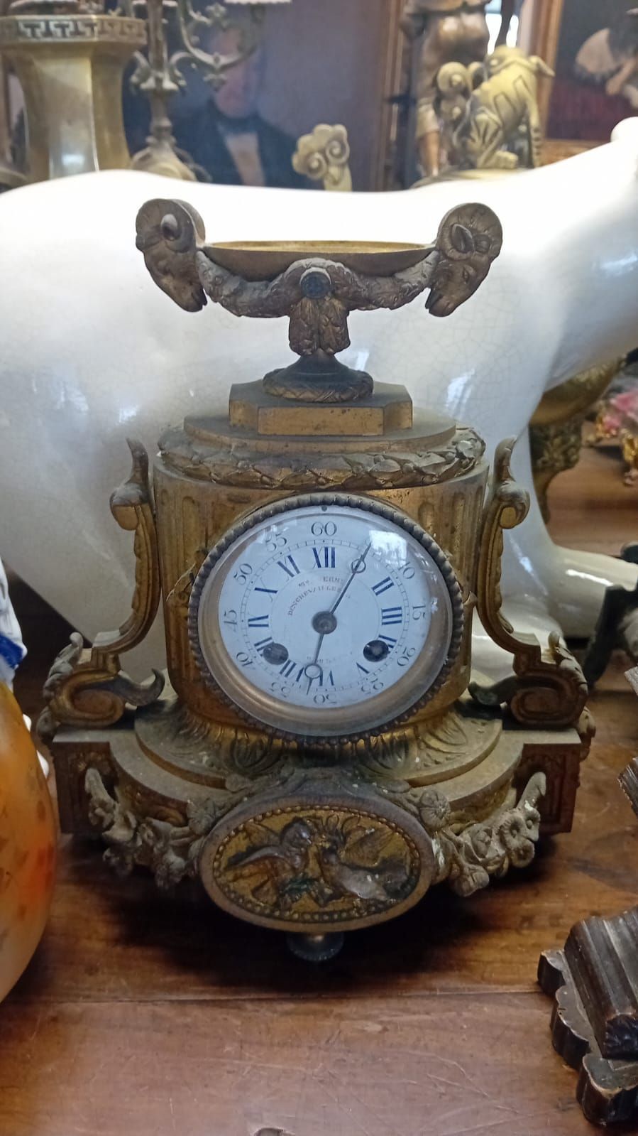 Horloge ancienne ornée, à cadran blanc, boîtier doré et détails décoratifs.