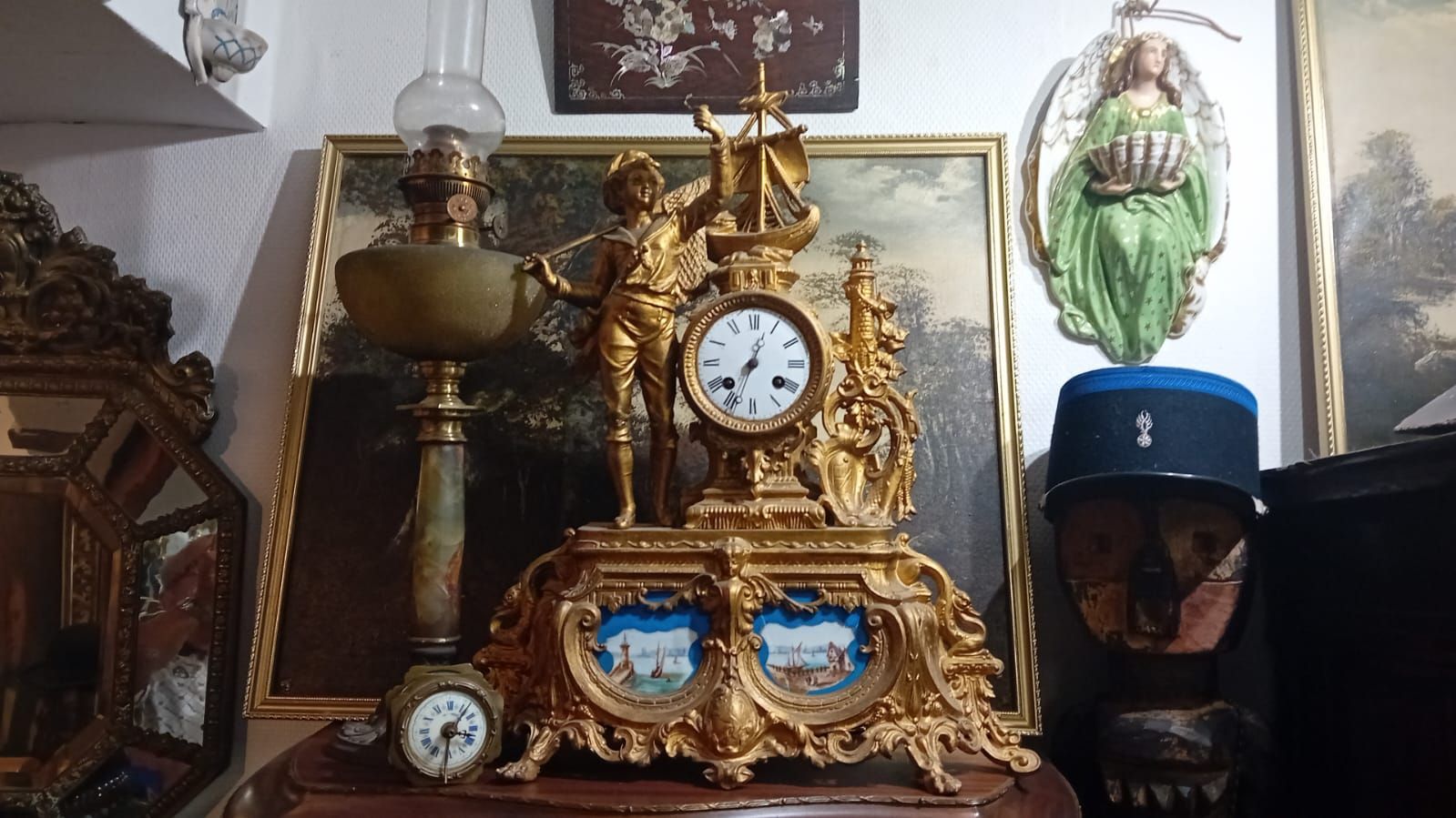 Horloge dorée ornée de figurines, lampe à huile, tableaux et casquette militaire.