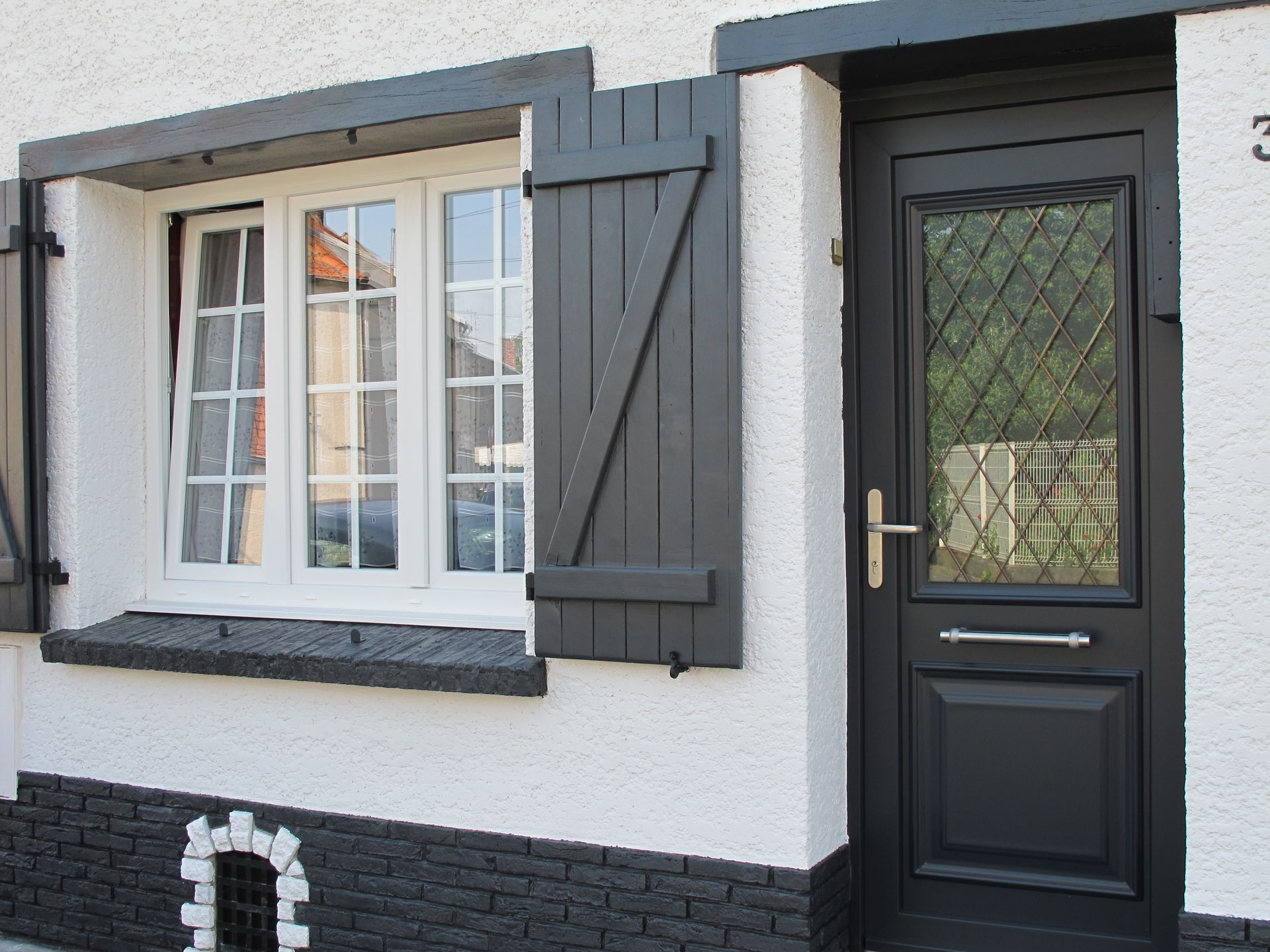 Porte d'entrée sombre, fenêtre blanche avec des volets battants