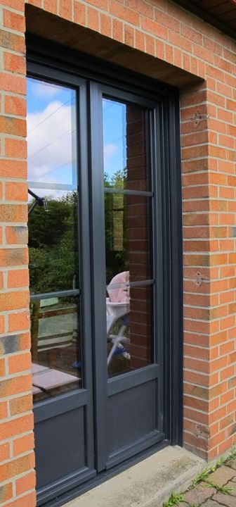 Porte vitrée à cadre gris encastrée dans un mur de briques rouges