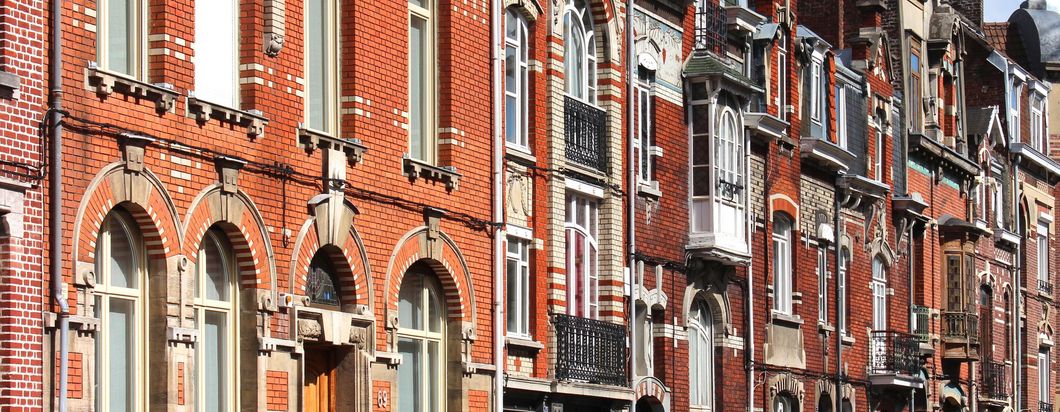 Une rangée d'immeubles traditionnels en briques, avec de hautes fenêtres, des arches décoratives en pierre et des balcons en fer forgé ouvragés.