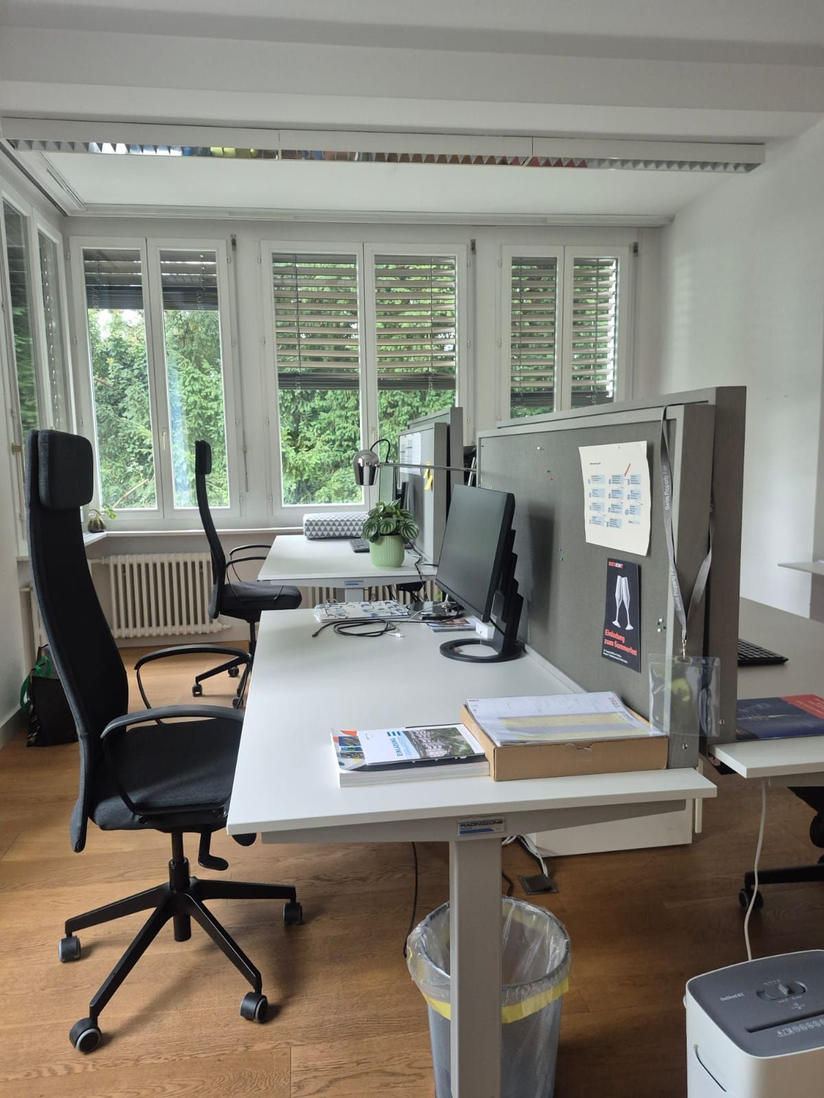 Eine Person reinigt mit einer Reinigungsmaschine eine nasse Holzterrasse in der Nähe eines Gebäudes, von Steinen und einem Topf.