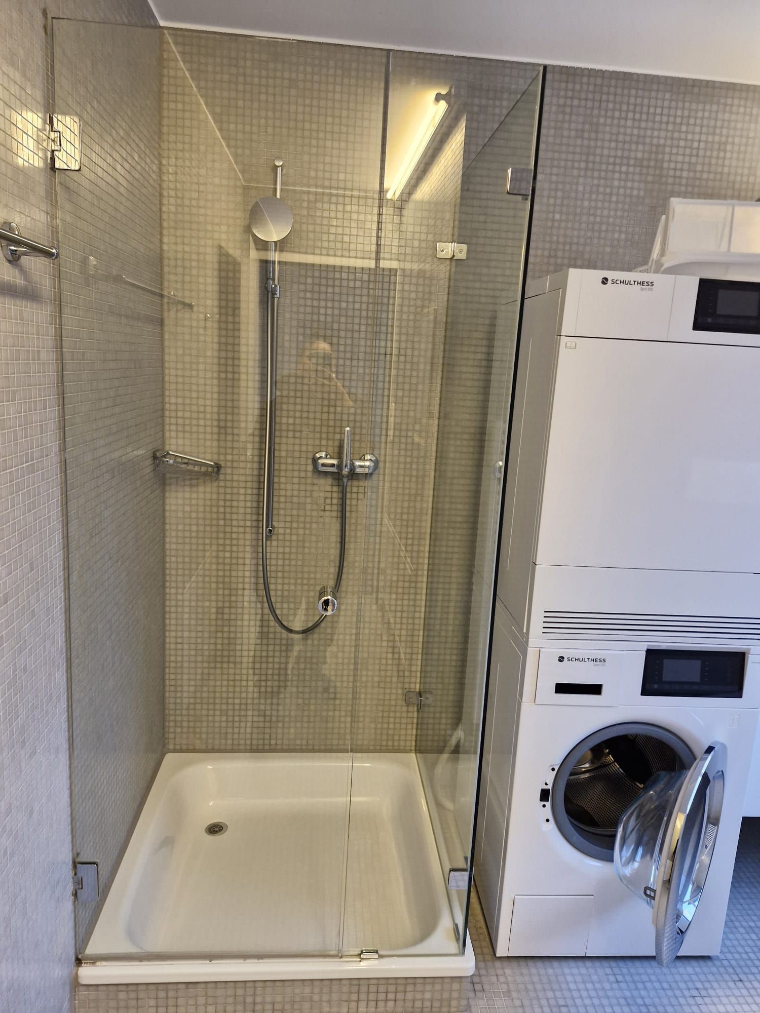 Balkon mit Glasschiebetüren, Steinboden, Topfpflanzen und Blick auf Häuser und Bäume an einem sonnigen Tag.