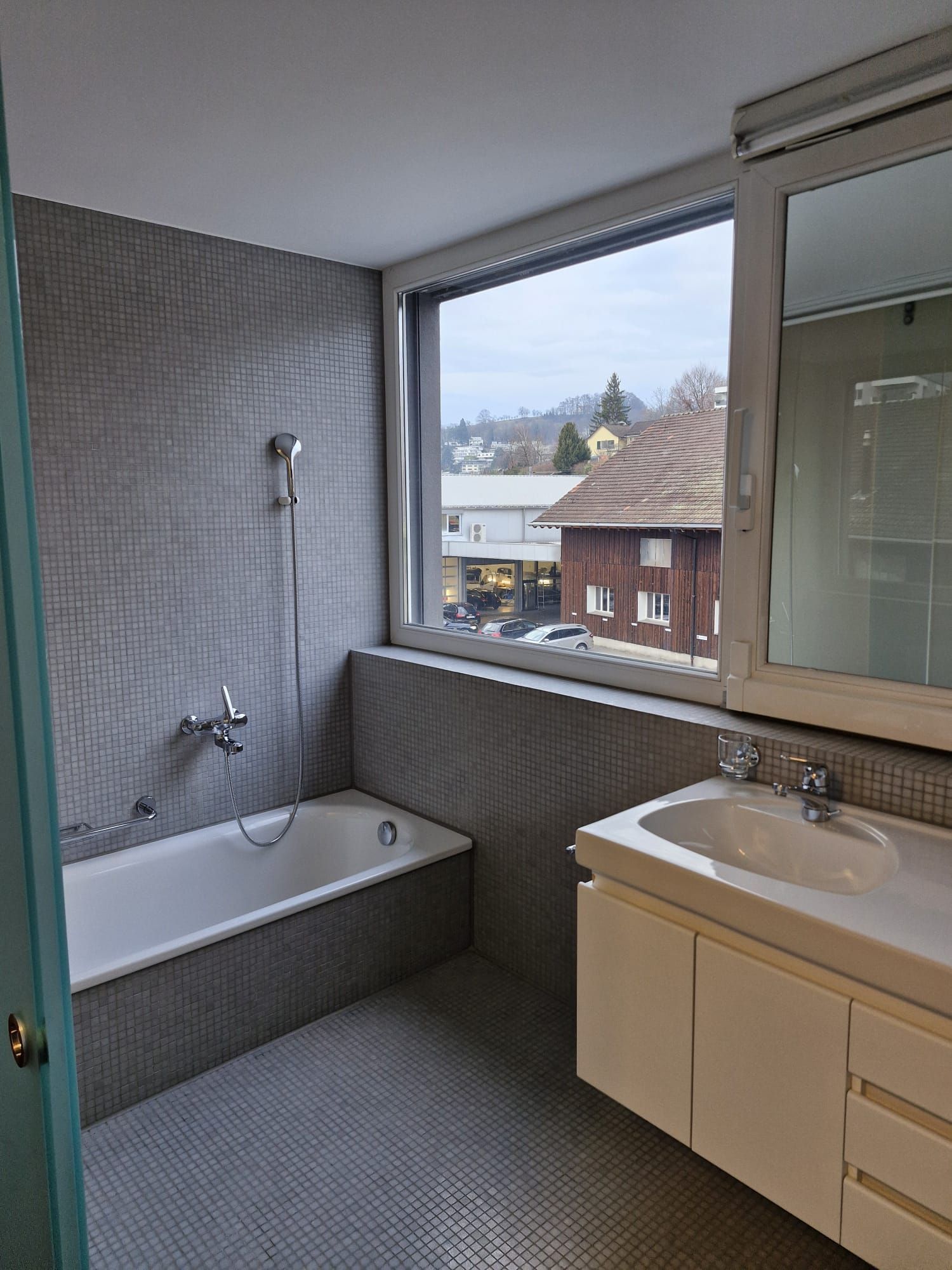 Ein Mann fegt an einem sonnigen Tag einen Kopfsteinpflasterweg neben einem Schaufenster aus Glas.