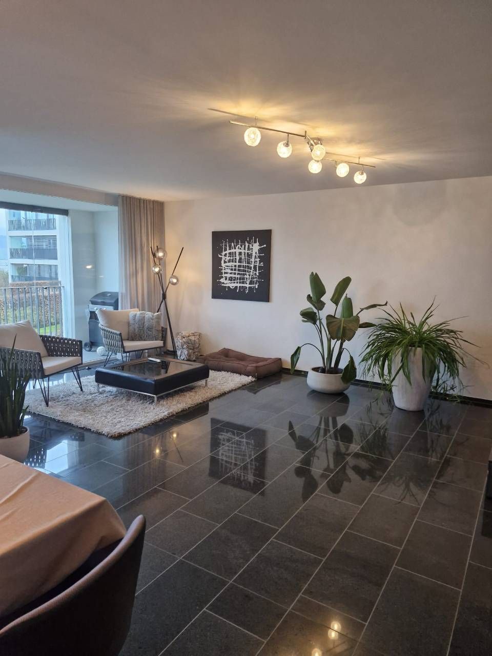 Modernes Wohnzimmer mit dunklem Fliesenboden, grossen Fenstern und zeitgenössischen Möbeln.