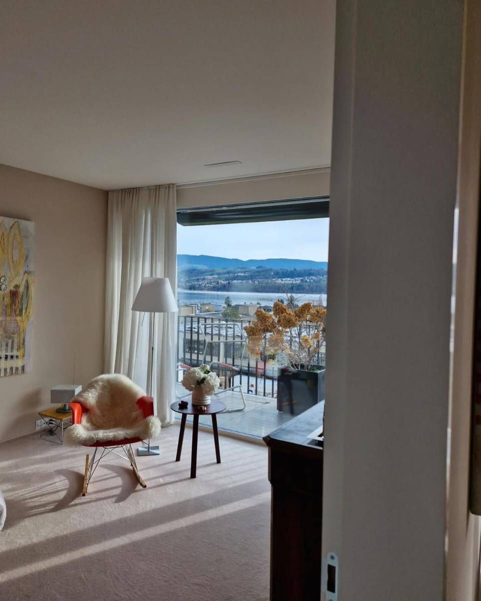 Innenraum mit Blick auf eine Wasserlandschaft. Lichtdurchflutet, mit einem Sessel und einem Tisch.