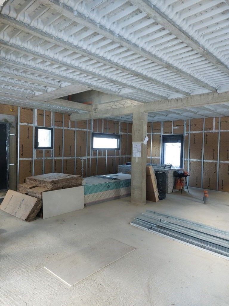 Un homme installe de l'isolant dans un mur en bois. Il porte des lunettes de sécurité, des gants et des vêtements de travail.