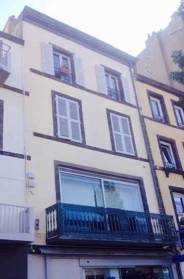 Un homme travaille sur un échafaudage, sur un bâtiment en pierre, avec un ciel bleu en arrière-plan.