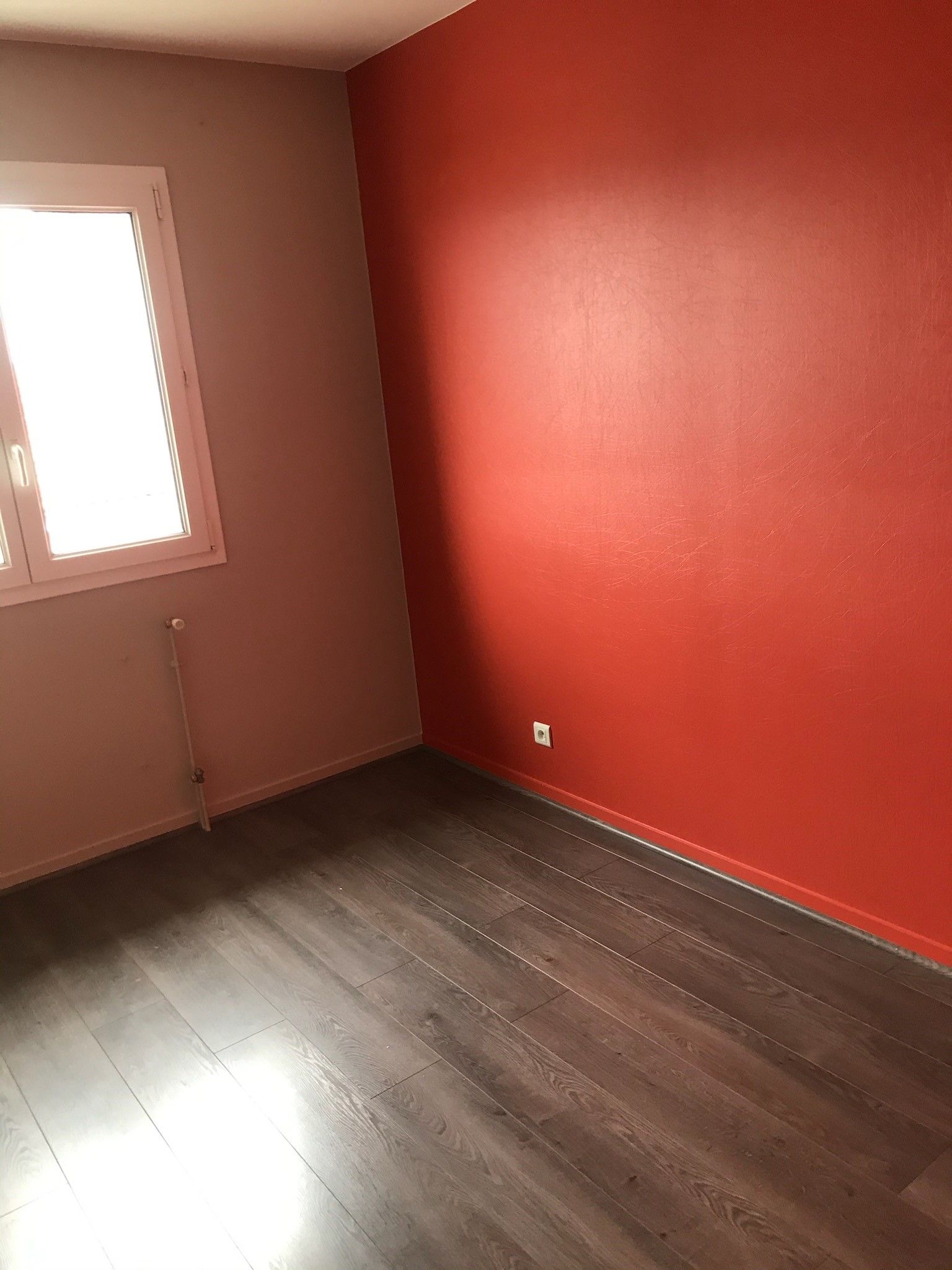 Une personne utilise un grattoir pour enlever l'excédent de matériau près d'un mur et d'une plinthe sur un sol d’imitation en bois.