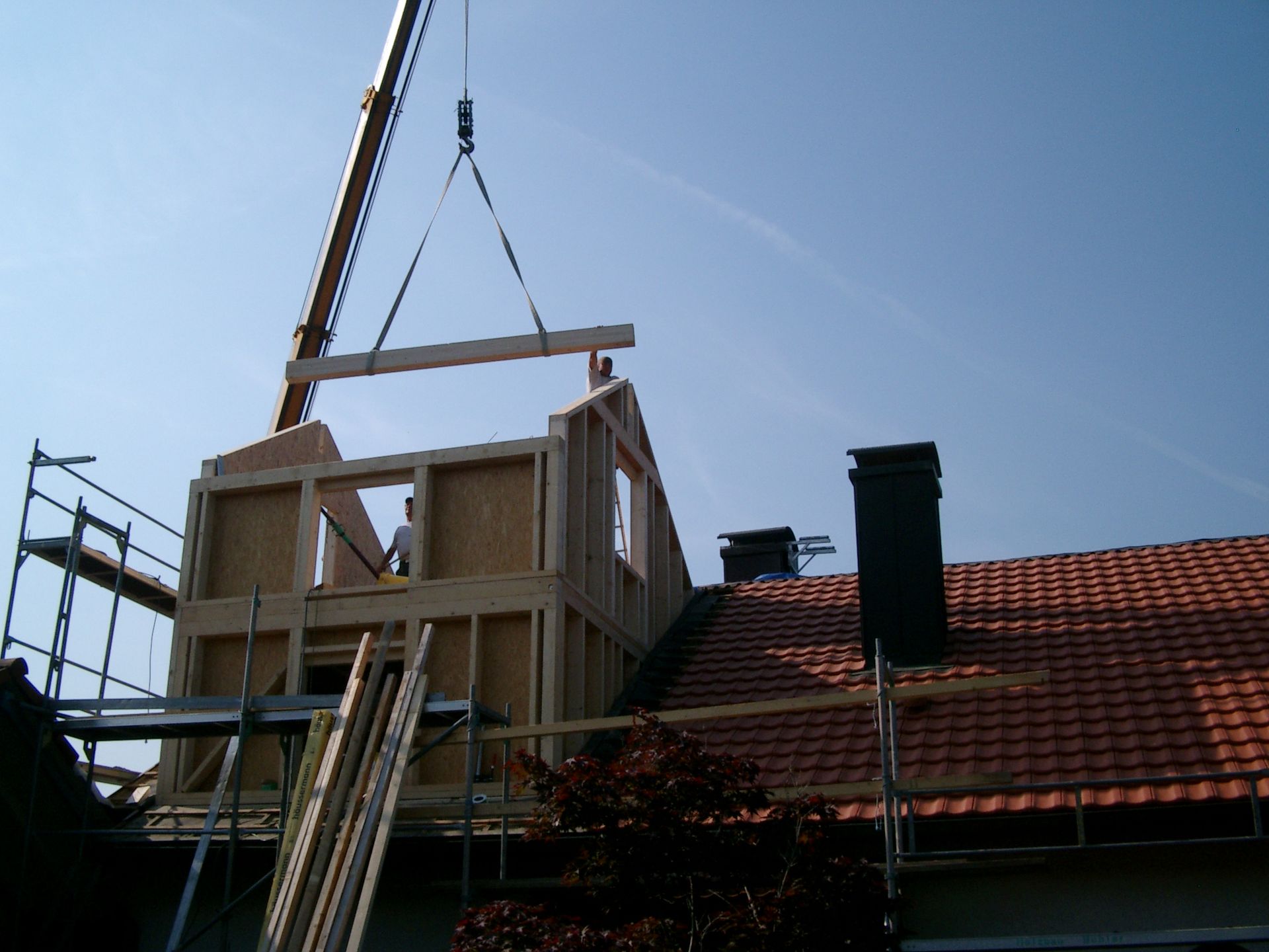 Ein Kran hebt eine Holzkonstruktion auf ein Haus