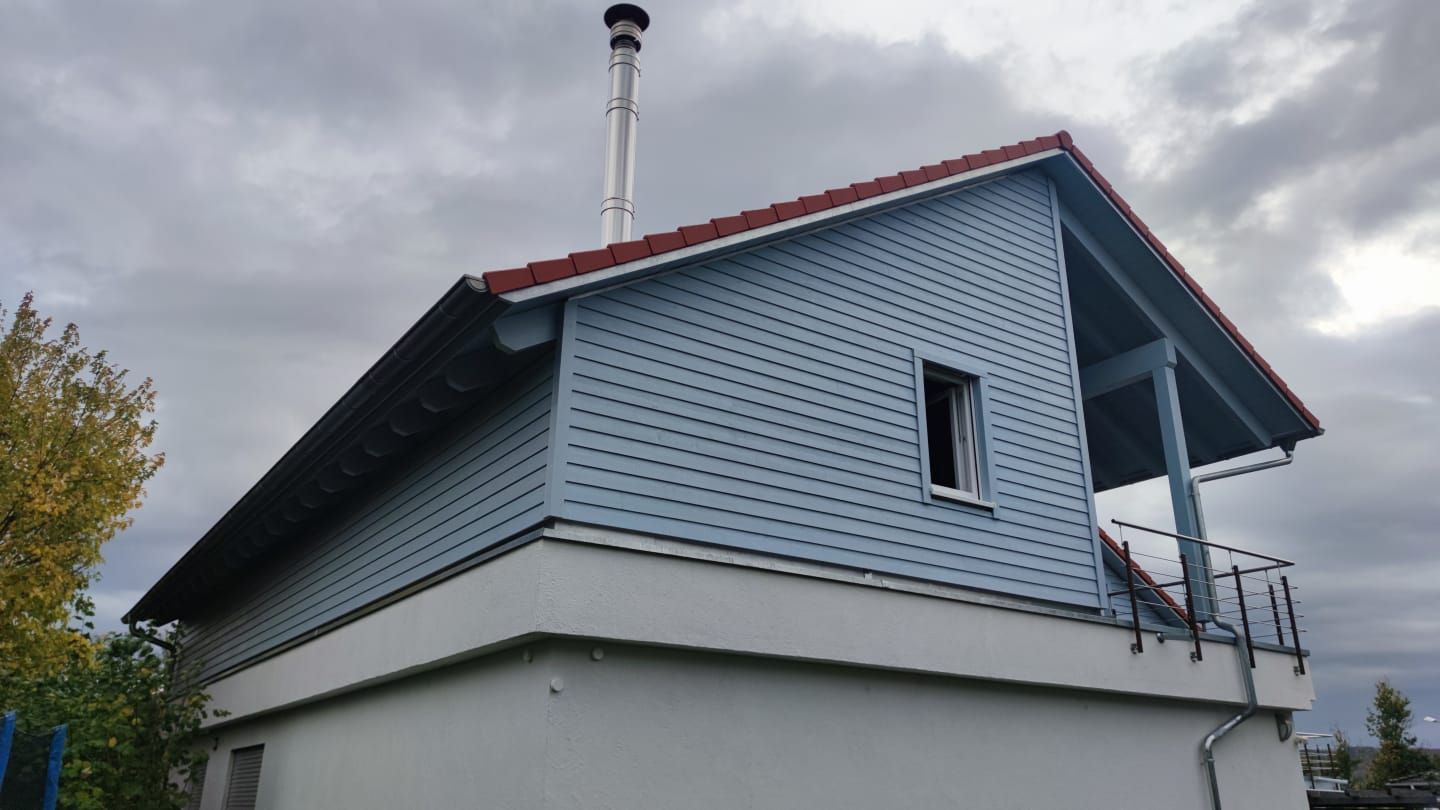 Ein blaues Haus mit einem roten Dach und einem Schornstein darauf.