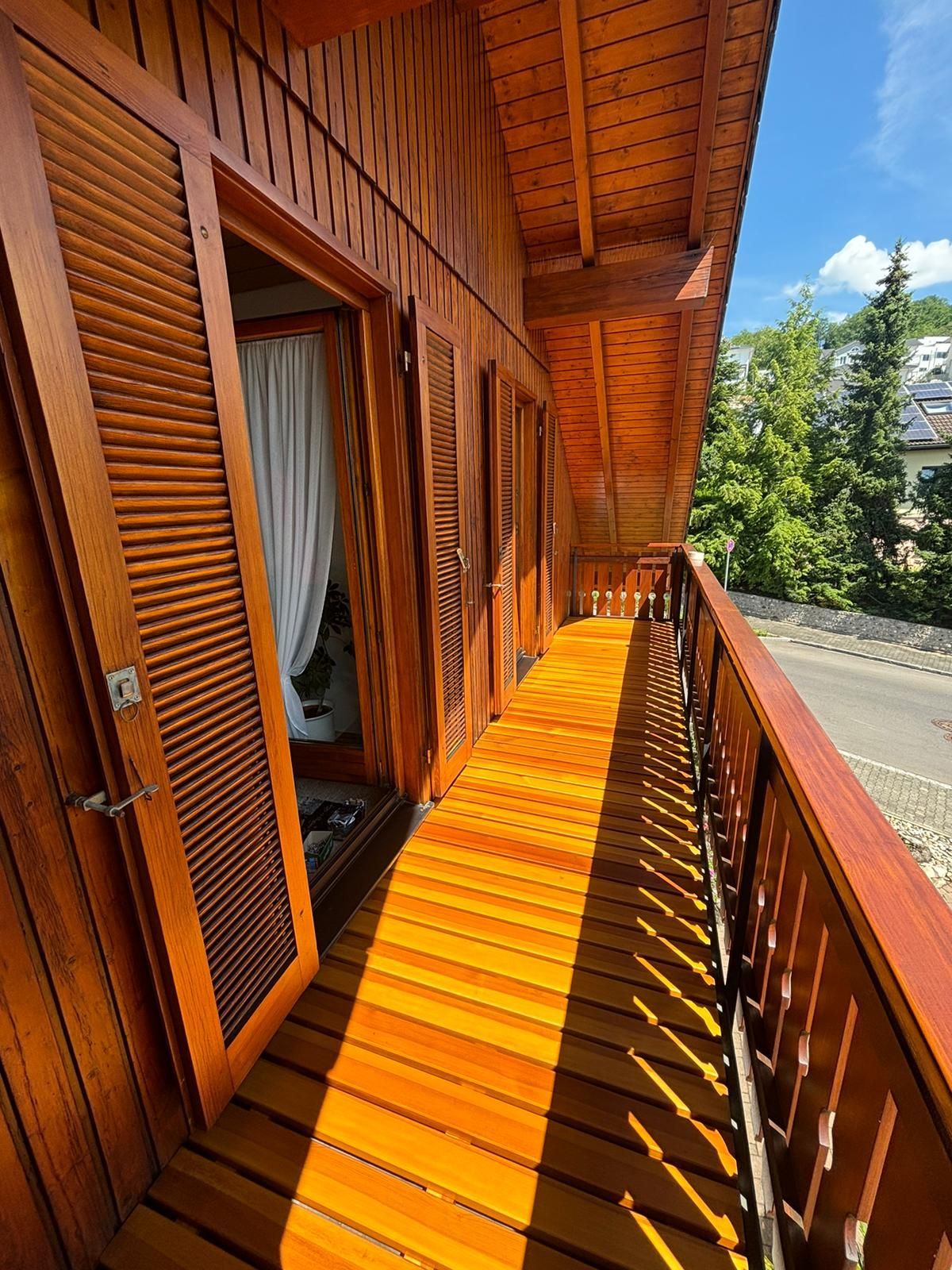 Ein Holzbalkon mit Holzboden und Fensterläden an einem Haus.