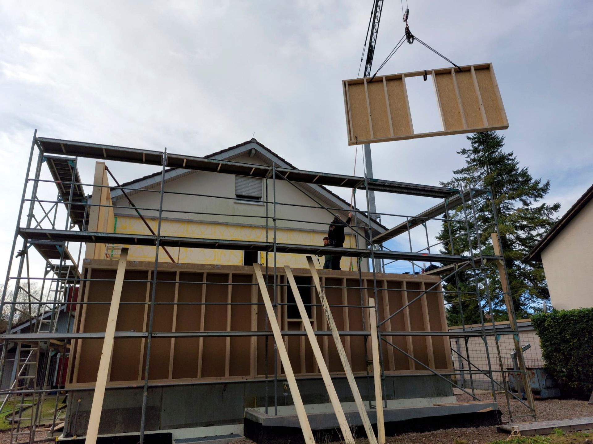 Ein Kran hebt ein Stück Holz über ein im Bau befindliches Haus.
