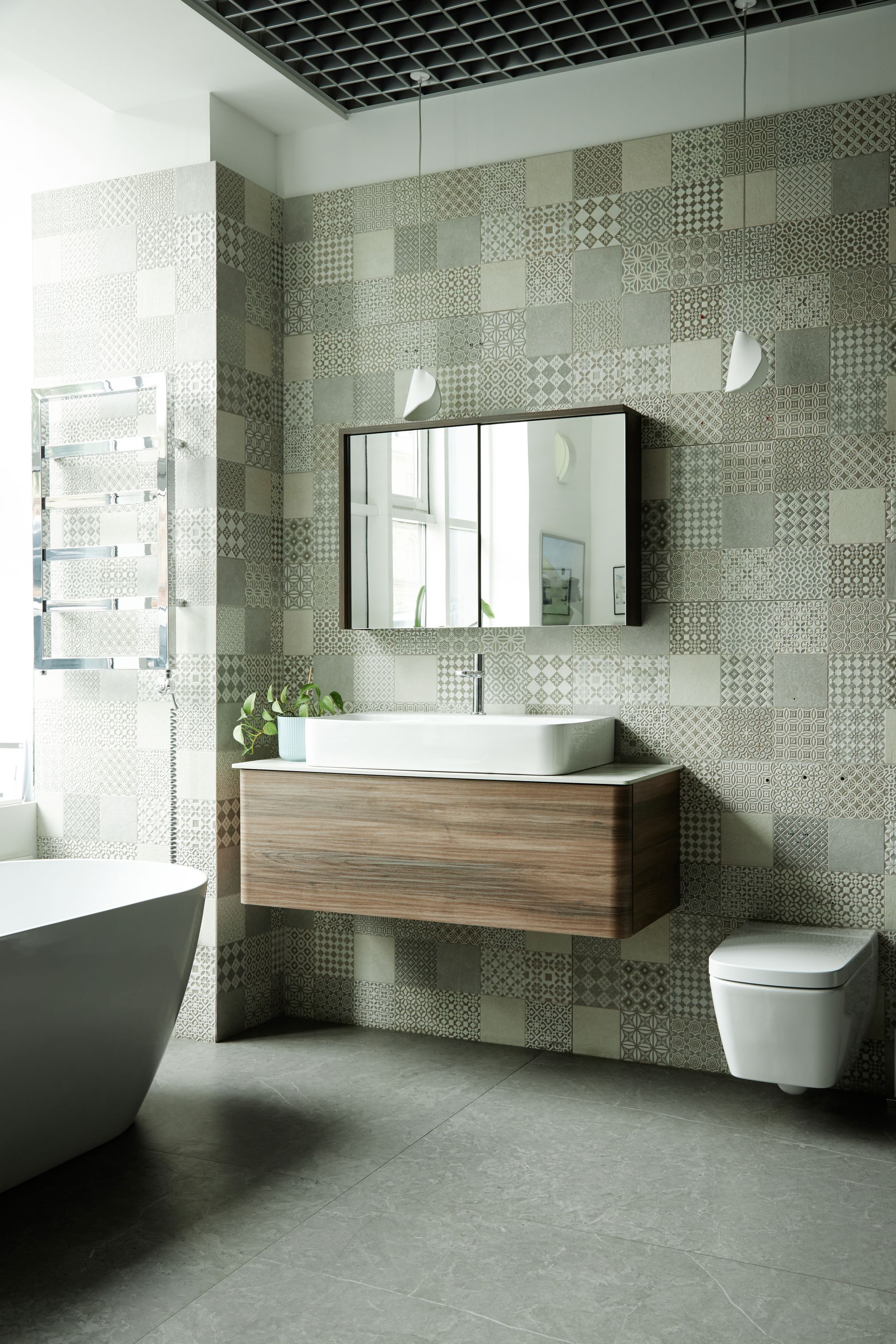 Salle de bains moderne avec mur à motifs, meuble sous lavabo suspendu en bois, lavabo blanc, miroir rectangulaire et toilettes.
