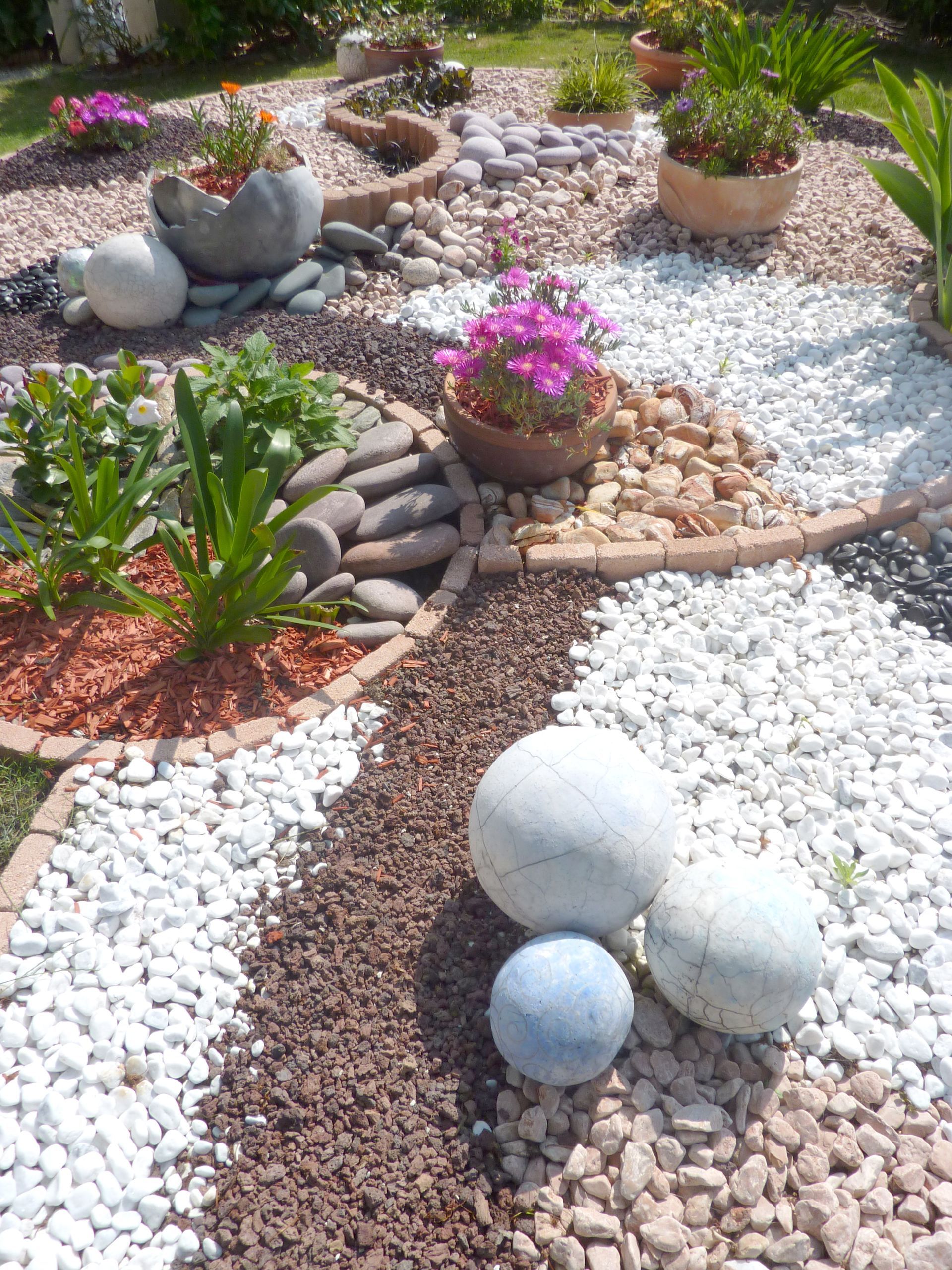 Un parterre coloré avec des allées de pierre, des pots de fleurs et des sphères décoratives.