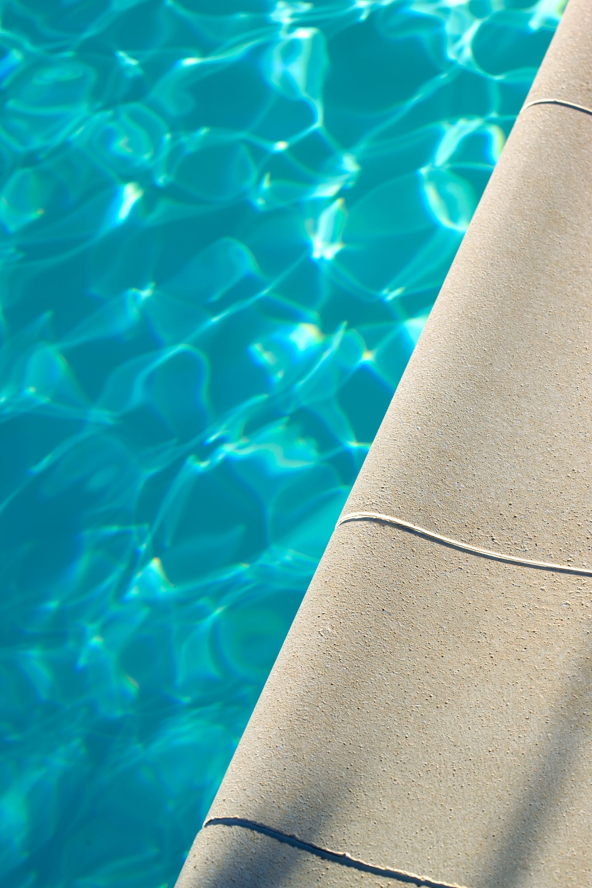 L'eau turquoise éclatante de la piscine côtoie un bord texturé gris clair.