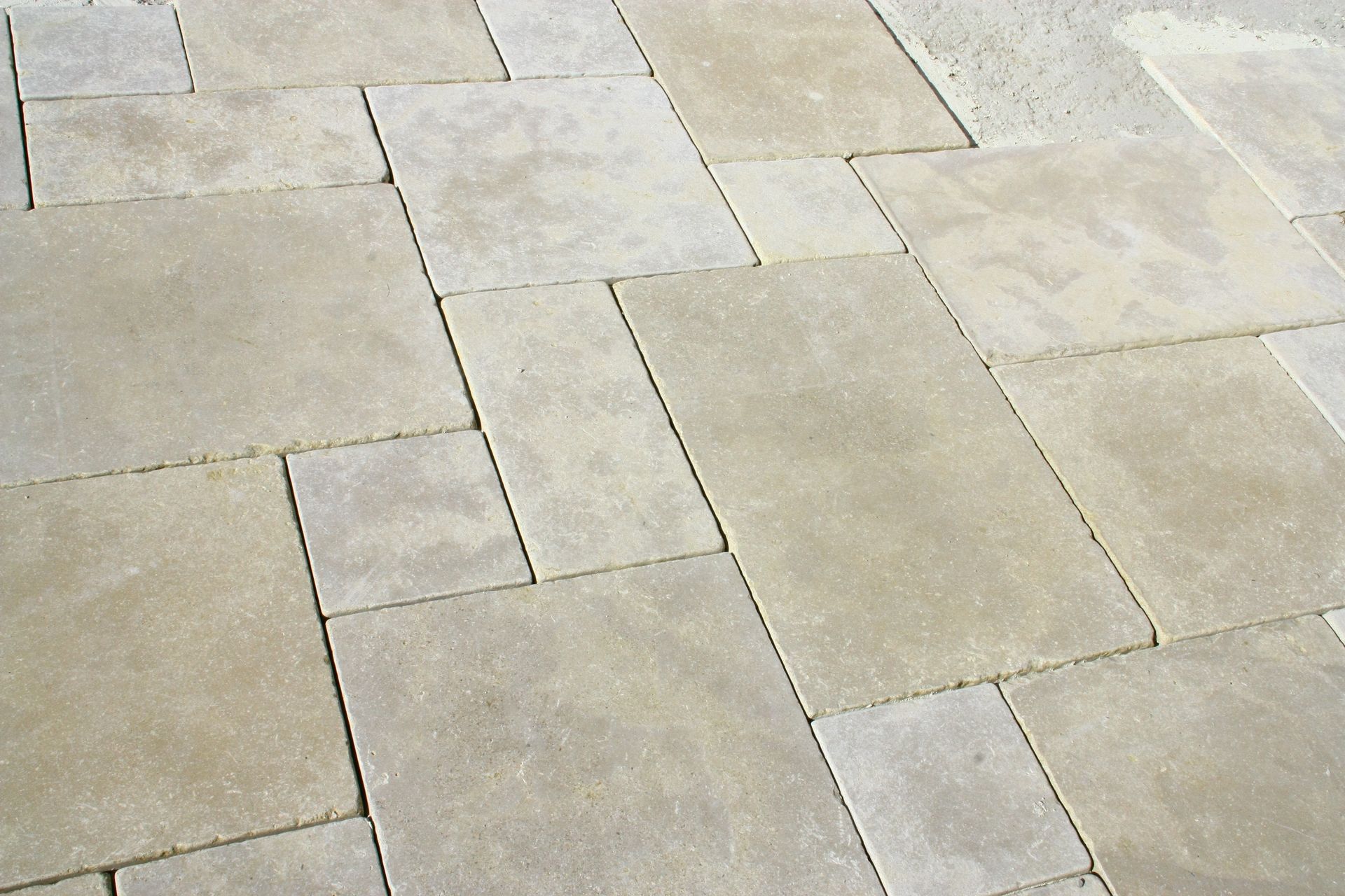 Dalles de terrasse en pierre beige disposées selon un motif rectangulaire varié.