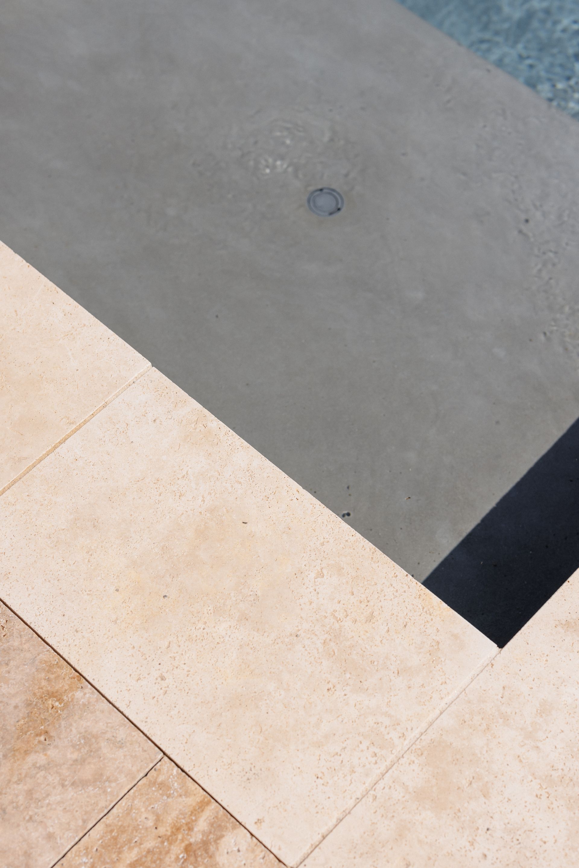 Escaliers d'une piscine aux bordures de carrelage beige et en béton gris menant à l'eau bleue.
