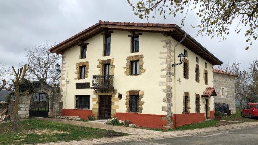Casa de dos pisos con paredes de estuco, molduras de piedra, detalles en rojo y una puerta marrón.