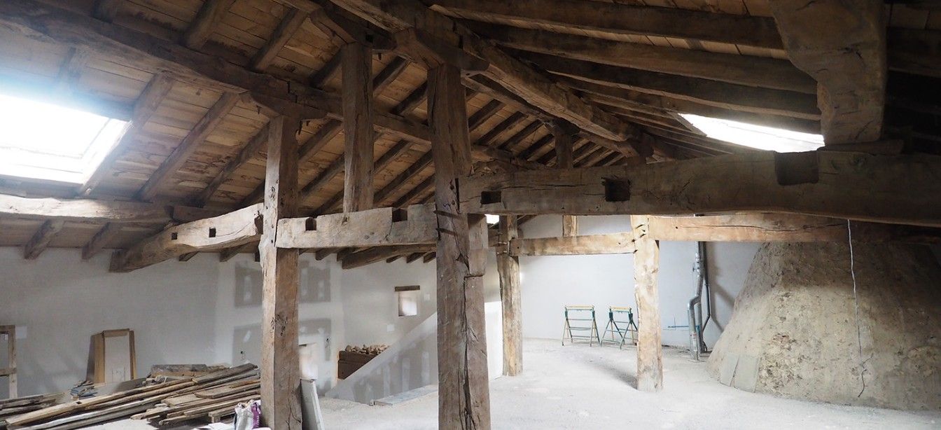 Interior de un edificio rústico con vigas de madera a la vista, un tragaluz y una gran pila de algo en el suelo.