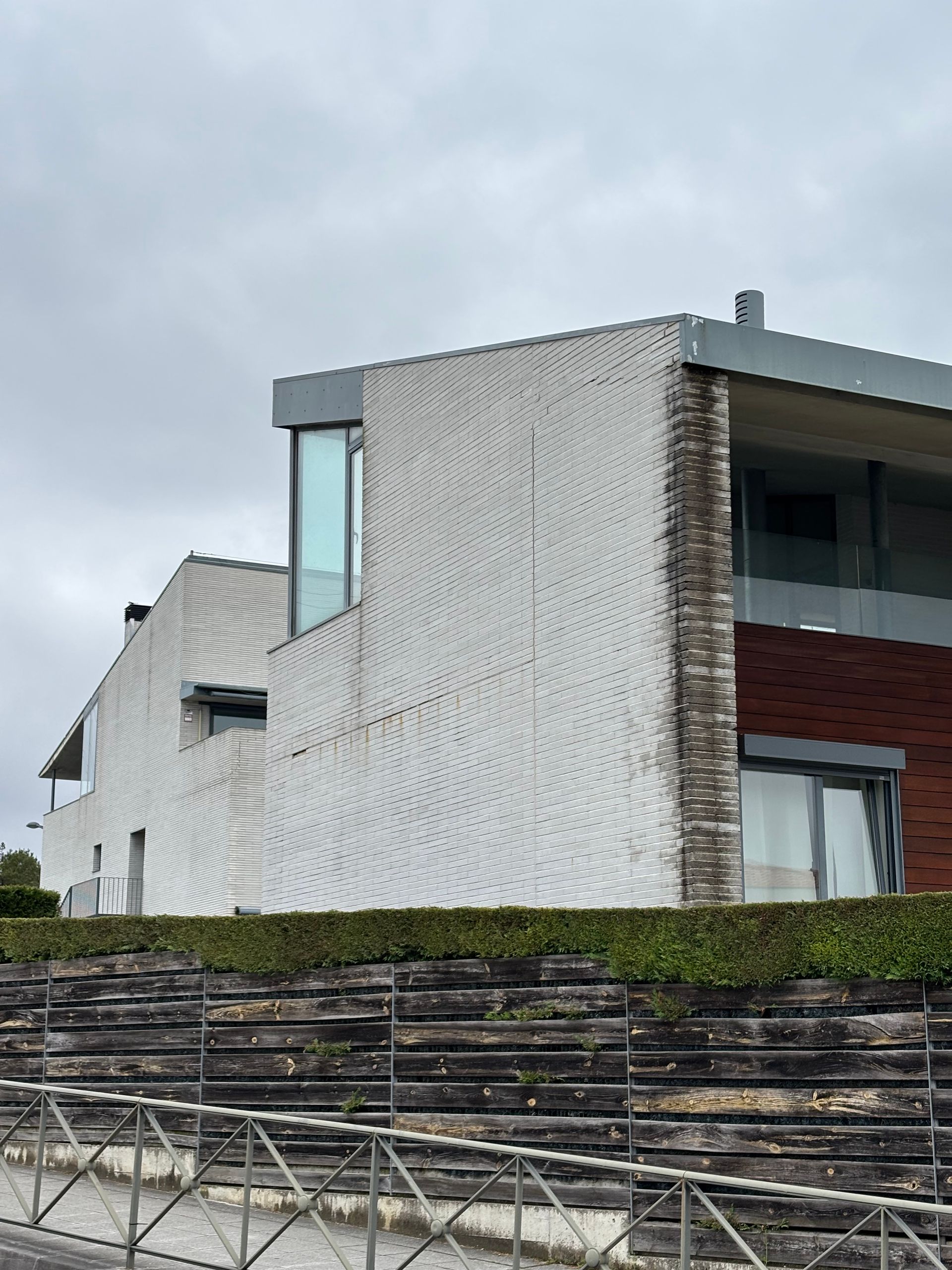 Edificio moderno con detalles de ladrillo blanco y ladrillo rojo, ventanas de vidrio y un seto verde.