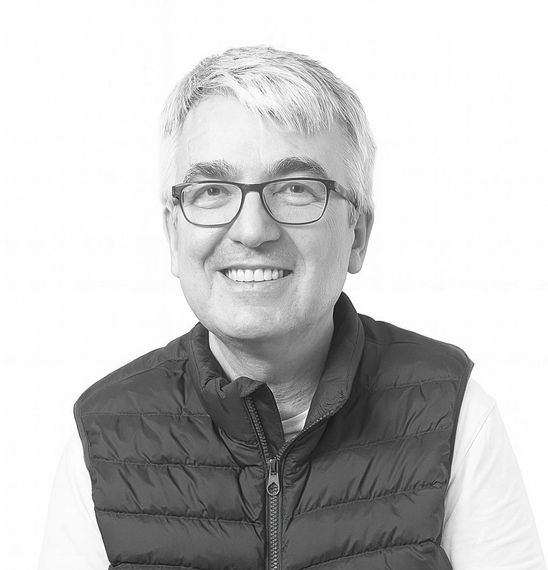 Hombre con gafas sonriendo, vistiendo un chaleco acolchado, delante de un fondo blanco.