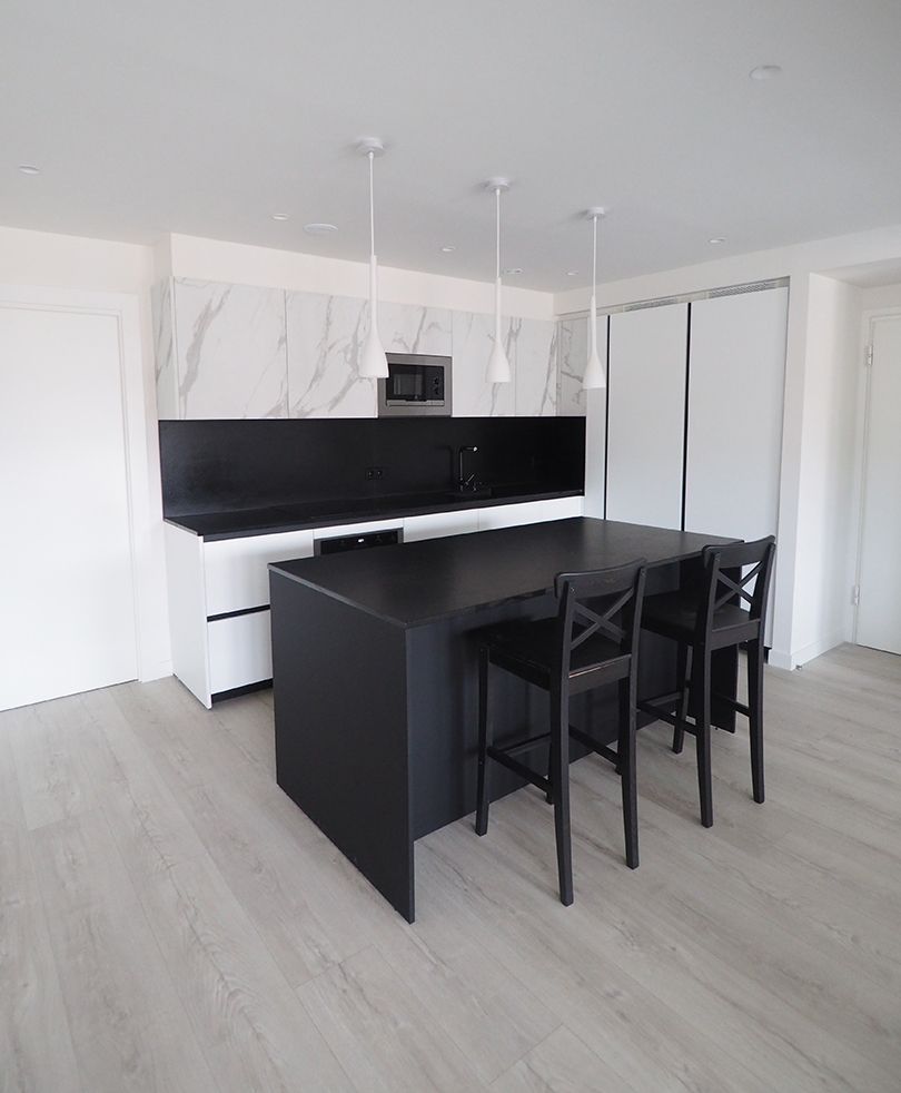 Cocina moderna con isla negra, gabinetes blancos, salpicadero de mármol y tres sillas negras.
