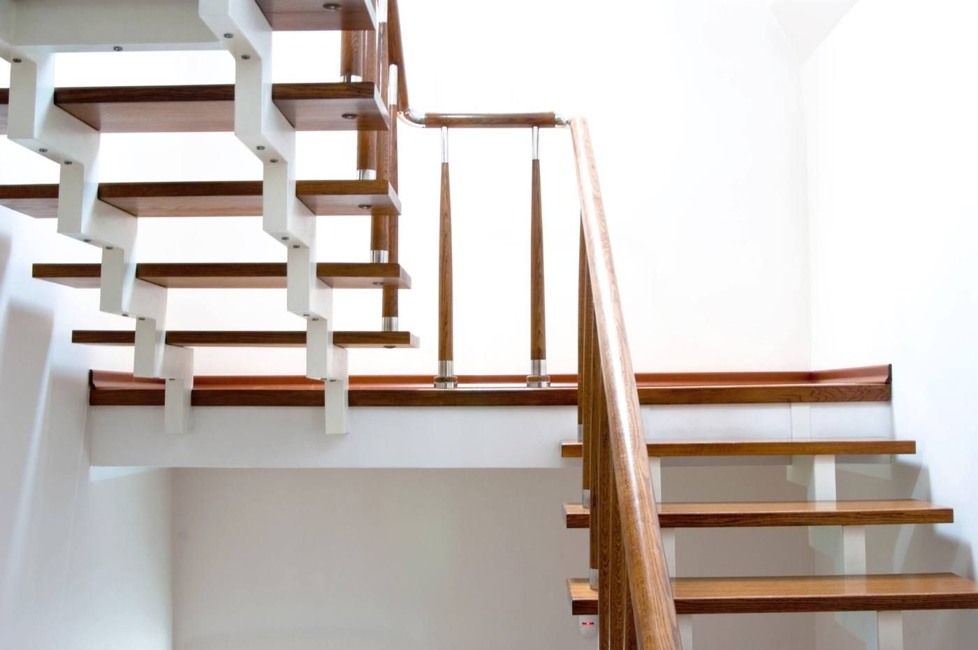 Escalera moderna de madera con contrahuellas blancas y pasamanos central en un interior luminoso.