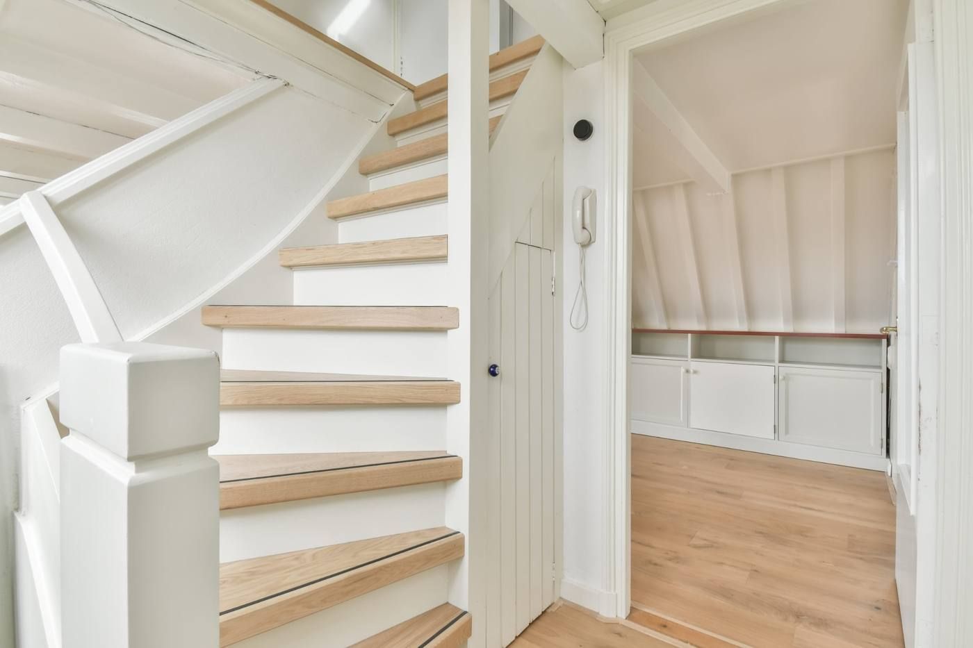 Una escalera de color blanco brillante se encuentra junto a una puerta que da a una acogedora habitación con suelo de madera.