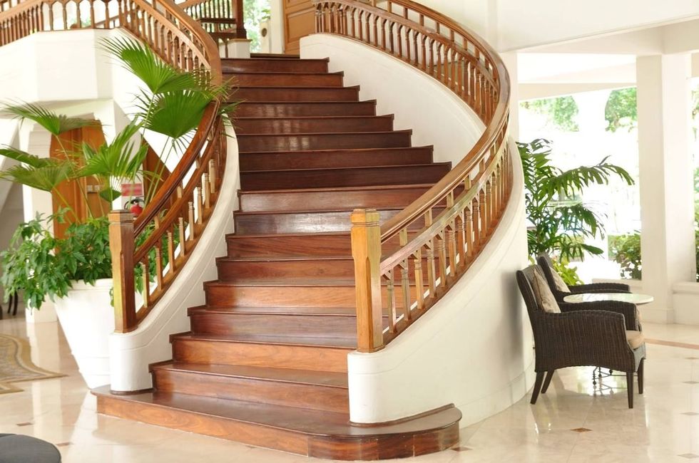 Escalera curva de madera con barandillas blancas en un vestíbulo luminoso de estilo tropical.