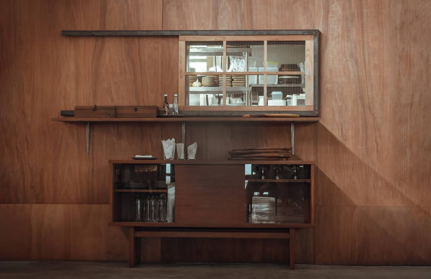 Mueble de pared de madera de mediados de siglo con vitrina, estantes y accesorios de bar en una habitación minimalista.