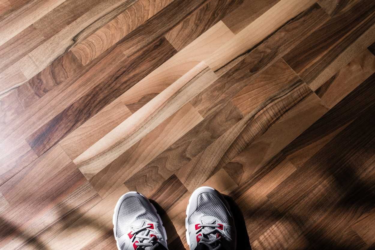 Zapatillas deportivas al borde de un suelo de madera con la luz del sol proyectando sombras diagonales.