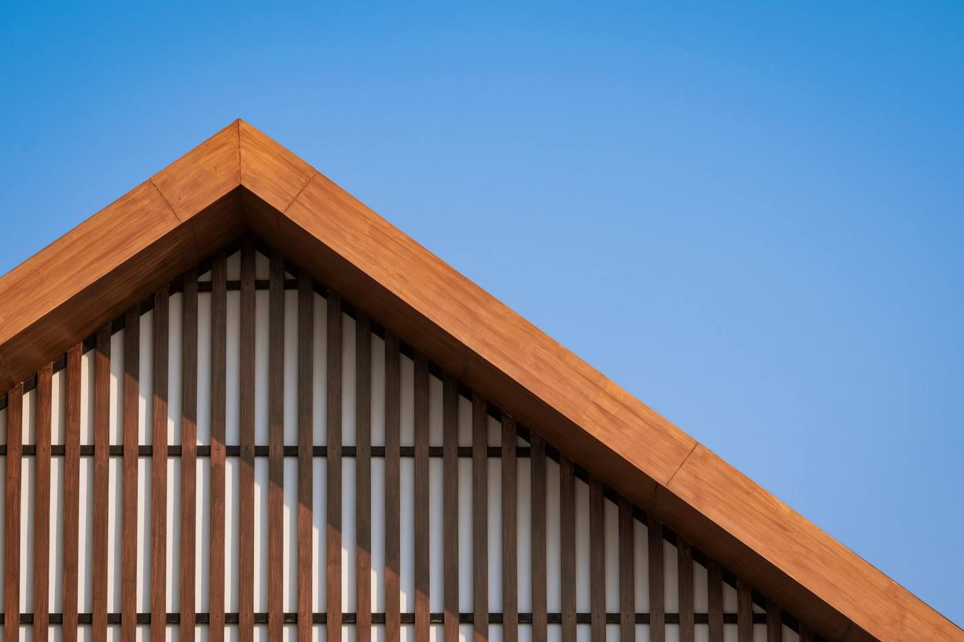 Tejado a dos aguas de madera con listones verticales contra un cielo azul claro