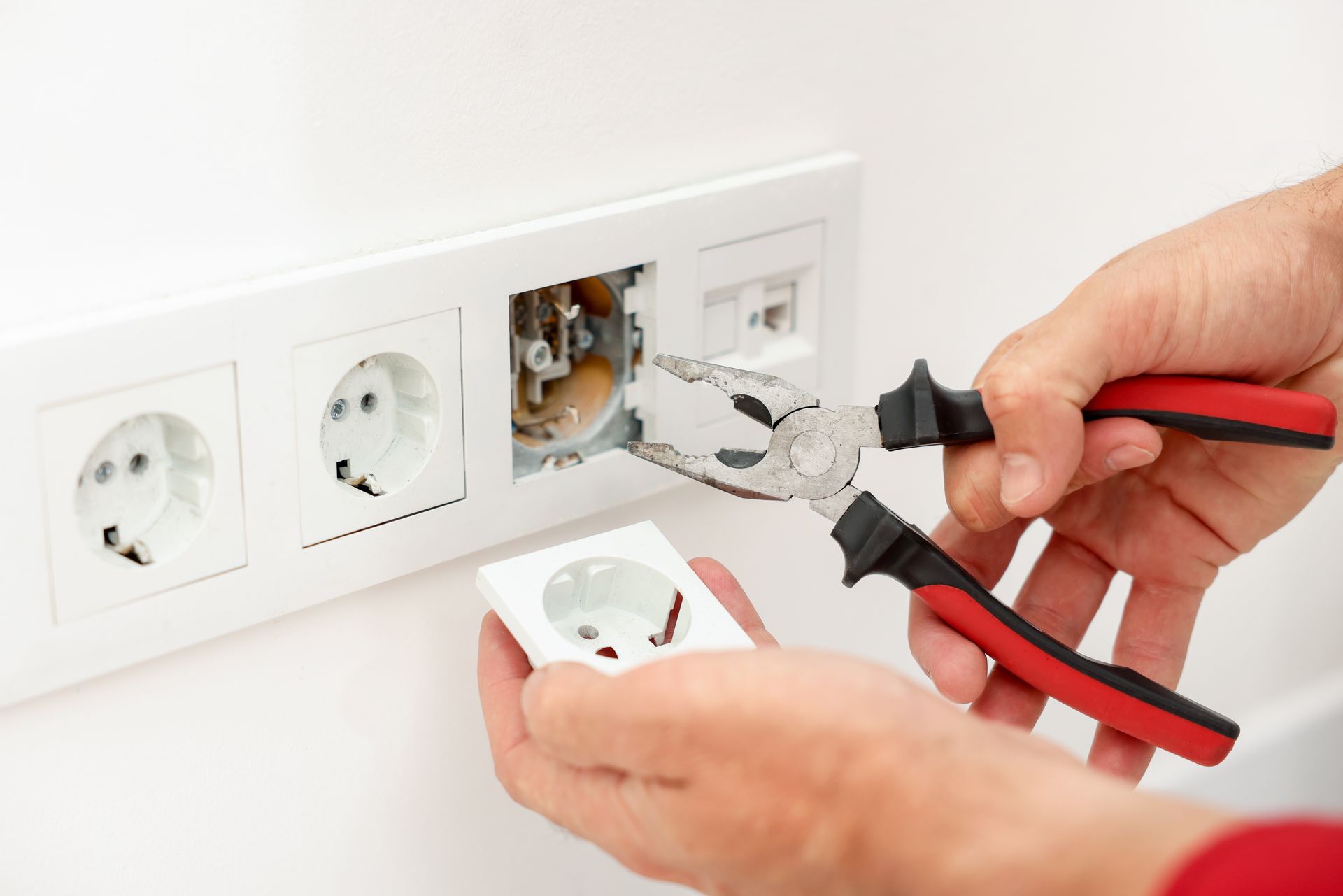 Mains utilisant des pinces pour installer une prise électrique sur un mur blanc.