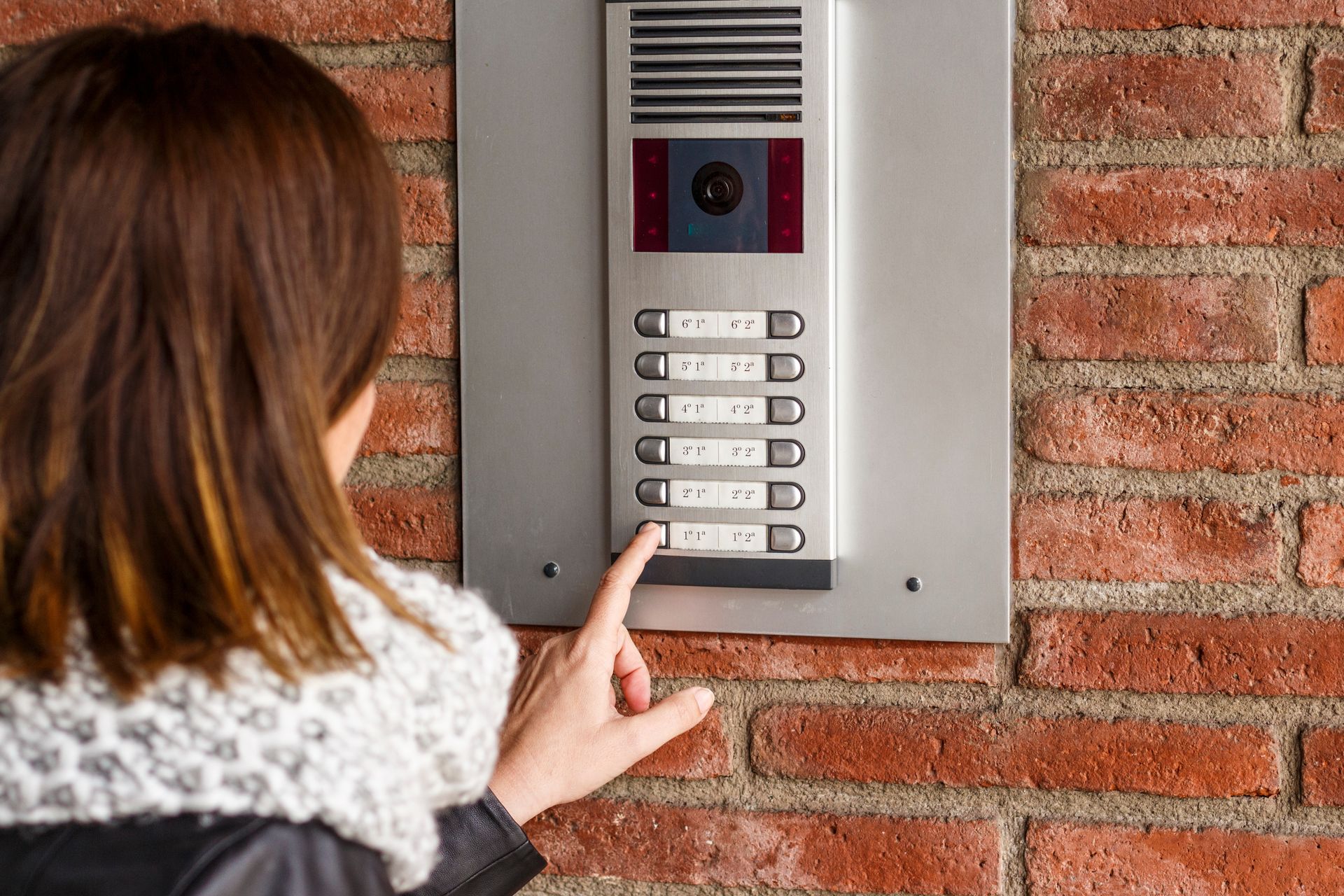 Une femme appuie sur un bouton d'un interphone sur un mur de briques.