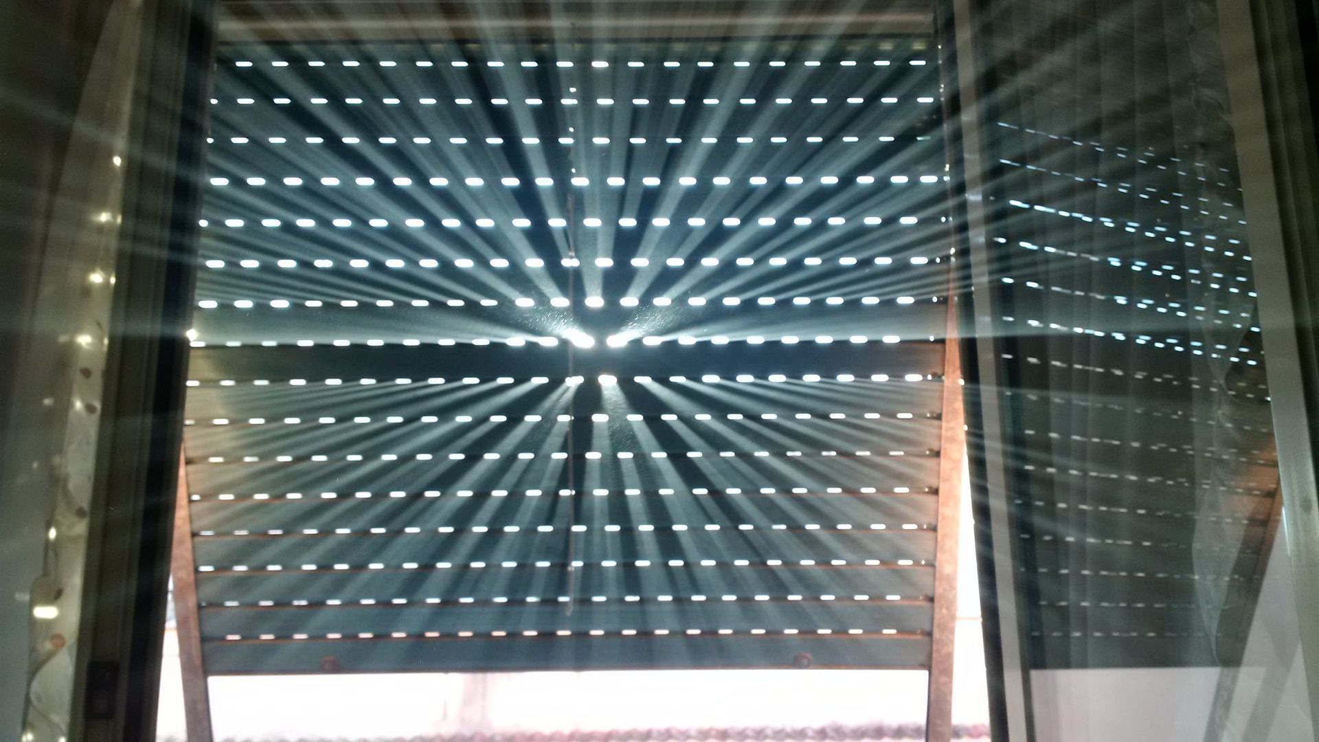 La lumière du soleil traverse un store à lamelles partiellement fermé.