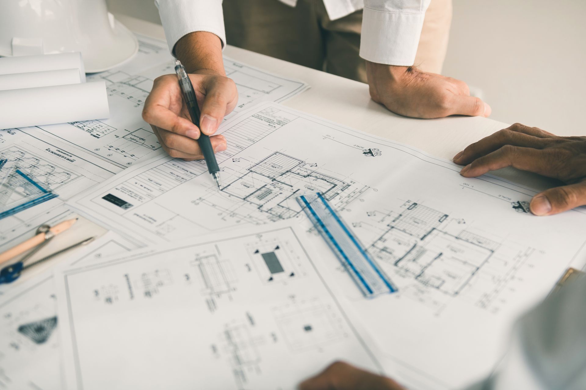 Des personnes examinant des plans architecturaux, pointant du doigt, avec des outils sur une table blanche.