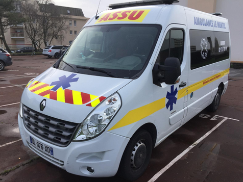Ambulance blanche TPMR avec marquages bleus, rouges et jaunes, garée à l'extérieur.