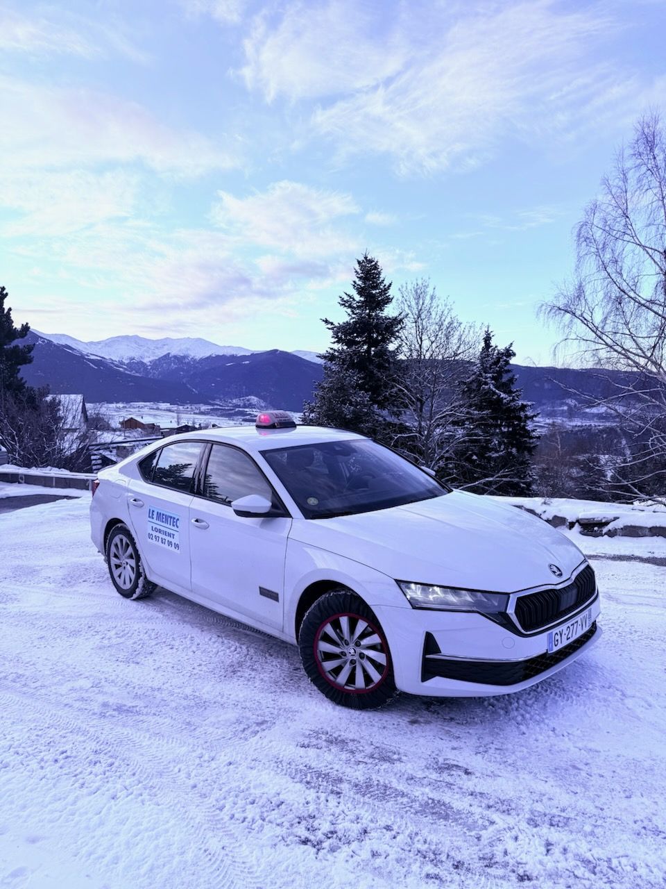 Voiture de taxi blanche sur un sol enneigé avec des montagnes en arrière-plan.