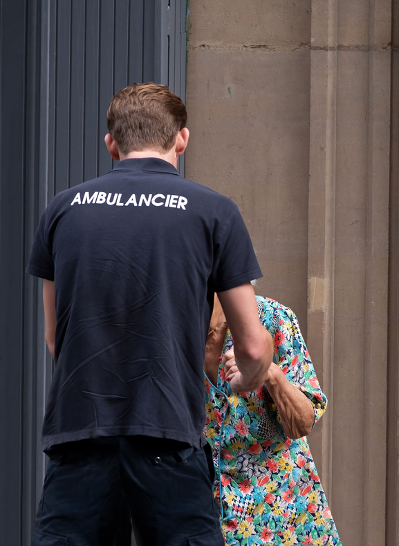 Homme en polo noir d'ambulancier aidant une personne agée.