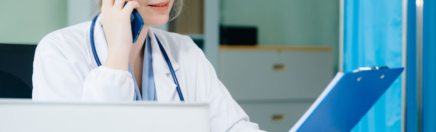 Un médecin en blouse blanche parle au téléphone tout en tenant un bloc-notes.