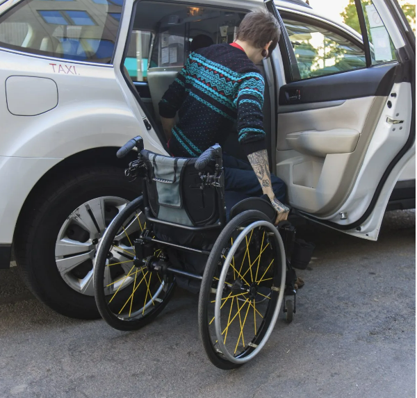 Personne entrant dans un taxi, avec un fauteuil roulant à côté.