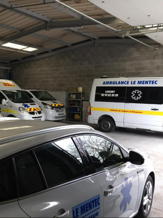 Ambulances garées dans un garage. Une voiture blanche est au premier plan.